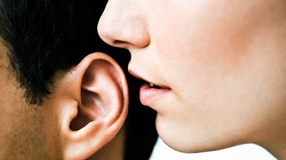 Eine Frau flüstert einem Mann etwas ins Ohr.