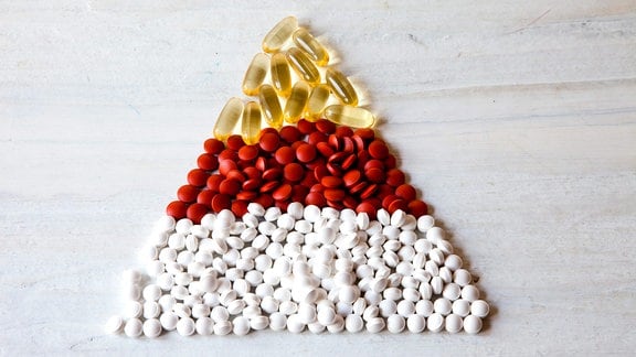 Tabletten in den Farben gelb, rot und weiß sind farblich in Schichten getrennt zu einem Dreieck gelegt.