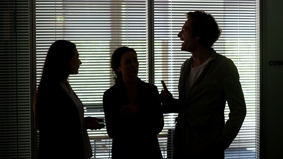Drei Kollegen stehen vor einem Konferenzraum in Berlin und unterhalten sich (gestellte Szene).