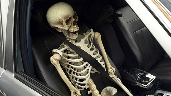 Ein Skelett sitz vorschriftsgemäß angeschnallt auf dem Beifahrersitz eines Autos.