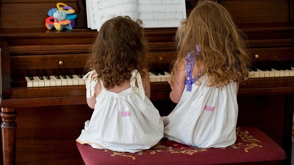 Zwei junge Mädchen in Kleidern spielen Klarvier