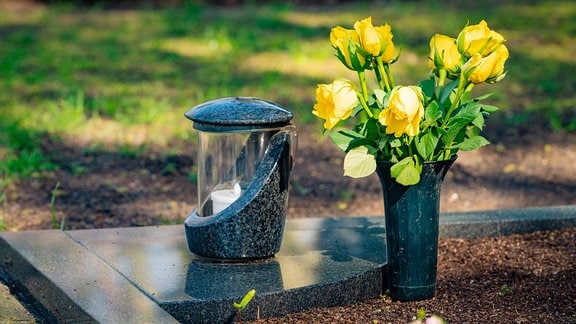 Eine Kerze und Blumen stehen auf einem Grab.