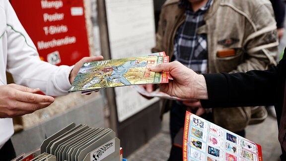Ein Mann verkauft einem anderen auf einem Flohmarkt ein Comic-Heft.