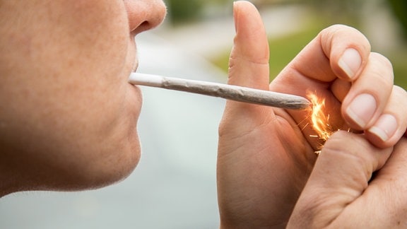 Symbolbild: Eine junge Frau zuendet sich eine selbstgedrehte Zigarette an (gestellte Szene).