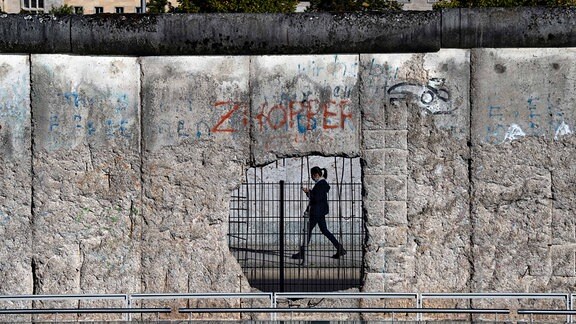 Eine Frau ist durch ein Loch der ehemaligen Grenzmauer an der Niederkirchnerstraße zu sehen