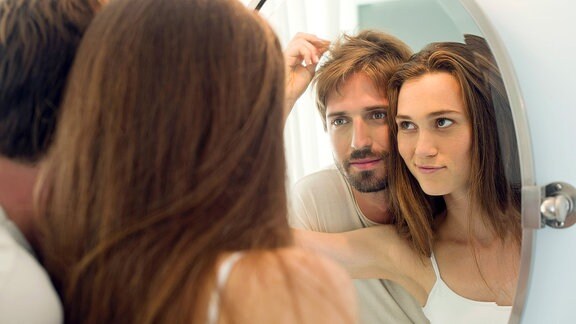 Ein Paar schauen sich ihre Haare in einem Spiegel an