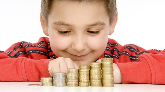 Ein Junge schaut auf einen Münzstapel vor sich