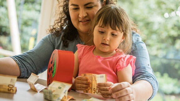 Ein kleines Maedchen hält Geldscheine in den Händen