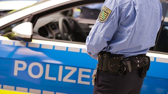 Ein Polizist steht vor einem Funkstreifenwagen