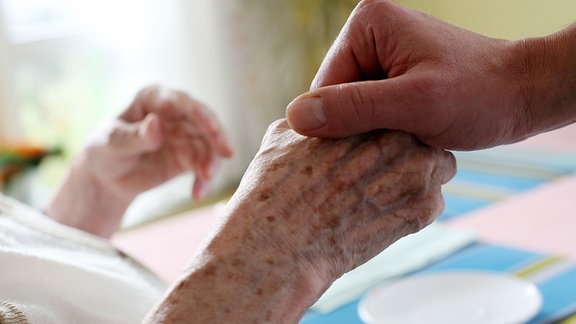 Ein Pfleger hält in einem Alten- und Pflegeheim die Hand einer Bewohnerin.