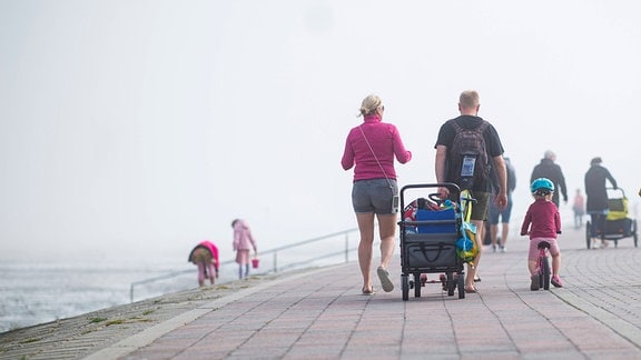 Eine Familie spaziert auf dem Deich entlang, links von ihnen liegt das Meer.