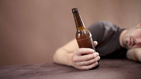 Betrunkener Mann schläft mit Bierflasche in der Hand.