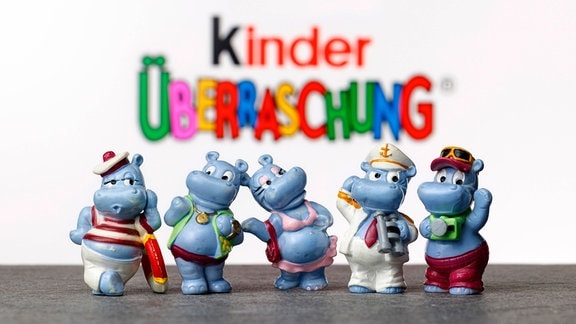 Überraschungseier-Figuren aus verschiedenen Serien der Happy Hippos vor einem Logo von Kinder Überraschung