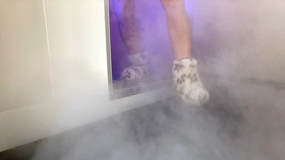 Füße in Kuschelschuhen kommen aus einem Raum, aus dem weißer Nebel steigt
