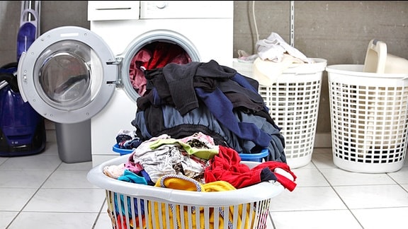 Übervolle Wäschekörbe vor einer Waschmaschine