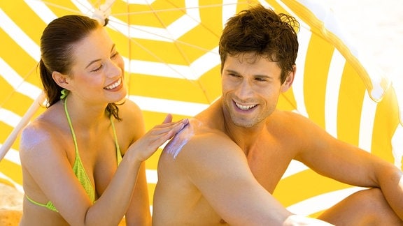 Eine Frau reibt ihren Freund mit  Sonnencreme ein. 