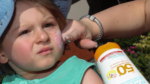 Auf das Gesicht eines Kleinkinds wird Sonnencreme mit LSF 50 aufgetragen.