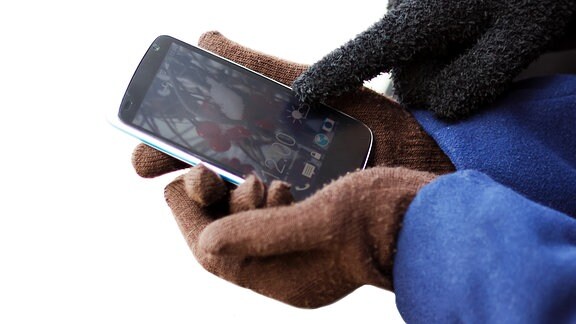ein Finger im Handschuh zeigt auf den Bildschirm eines Smartphones