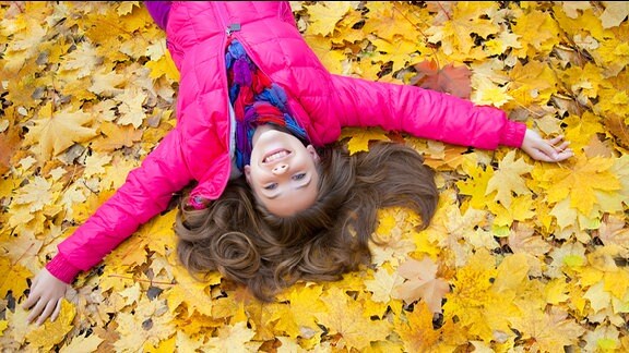 ein Mädchen liegt im Herbstlaub und lacht.