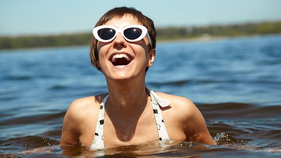 eine junge Frau badet lachend im See