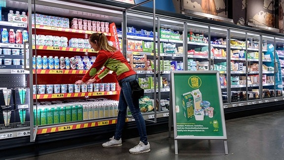Eine Supermarktmitarbeiterin räumt ein Kühlregal ein