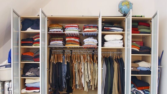 Kleiderschrank eines Mannes. Bekleidung aller Art hängt und liegt in verschiedenen Schrankfächern.