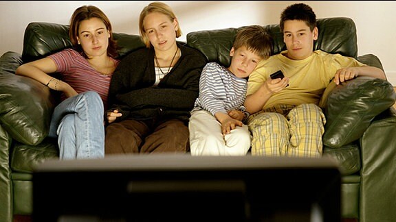 Kinder sitzen auf einer Couch und schauen Fernsehen
