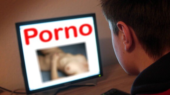 Symbolbild zum Internet Konsum von Kindern und Jugendlichen, die auch immer früher auf Sex Internetplattformen zugreifen: Jugendlicher sitzt am Bildschirm eines PC s mit Schriftzug Porno und dem Bild einer nackten Frau
