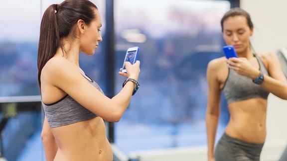 Eine Frau macht im Fitnessstudio ein Selfie mit ihrem Smartphone.