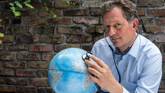 Dr. Eckart von Hirschhausen mit Stethoskop an einem Globus