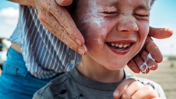 Kind bekommt Sonnencreme aufs Gesicht aufgetragen