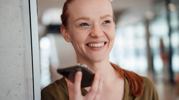 Eine lächelnde Frau hält ein Smartphone in der Hand.