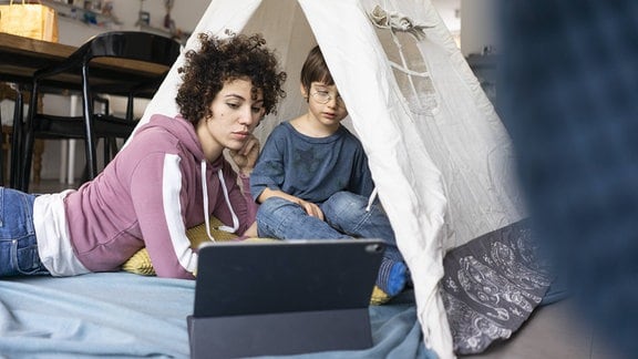 Eine Mutter und ein Kind sitzen in einem Spielzelt und schauen einen Film auf einem Tablet.